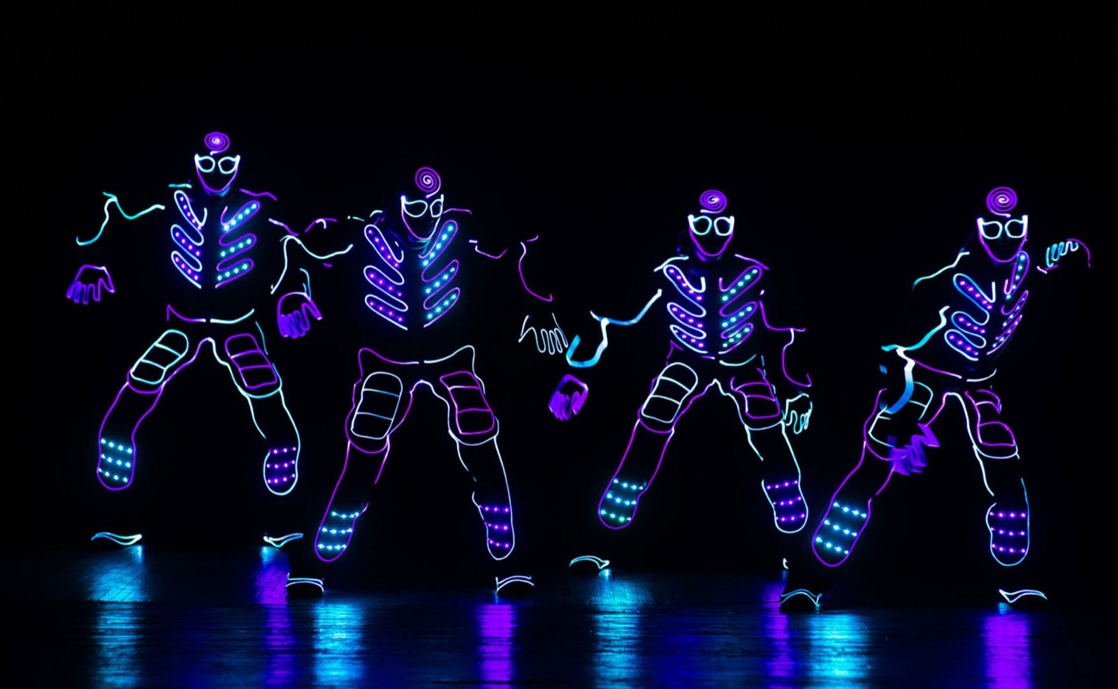 Four LED dancers in glowing suits on a dark stage